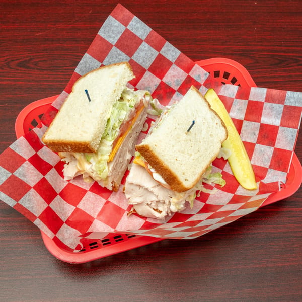 A turkey sandwich with cheese, lettuce, and tomato, cut in half, served with a pickle spear.