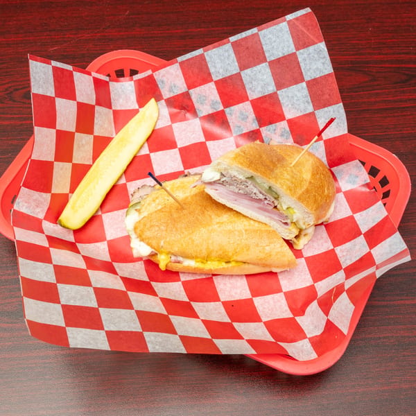 Cuban sandwich with ham, pork, cheese, mustard, and pickles, served in a red basket.