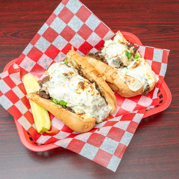 Two cheesy steak and mushroom subs with green peppers and a pickle spear in a red basket.