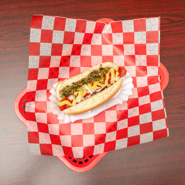 Hot dog with mustard, ketchup, relish, and onions in a red checkered basket liner.