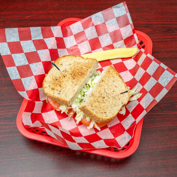 Toasted sandwich with lettuce and tomato, cut in half, served in a red basket with a pickle spear.